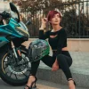 Confident woman with red hair sitting by a motorcycle in the city, exuding a strong modern vibe.